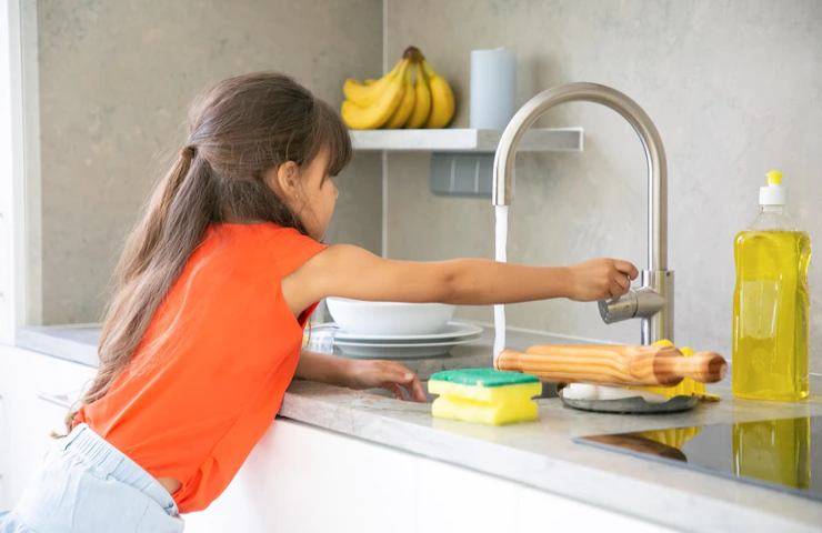 Una bambina apre l'acqua in cucina