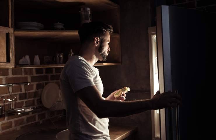 A man in front of the open fridge at night.