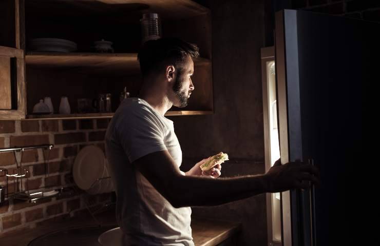 Un uomo davanti al frigo aperto di notte