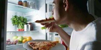 Un uomo in giovane età addenta una pizza di notte