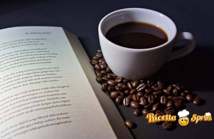 Una tazza di caffè su dei chicchi e con un libro accanto