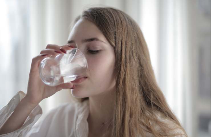 Una ragazza beve un bicchiere di acqua potabile