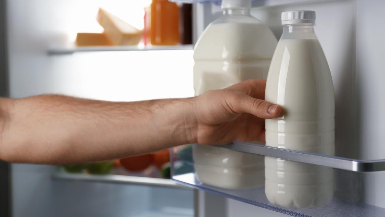 Uomo prende bottiglie di latte in frigo