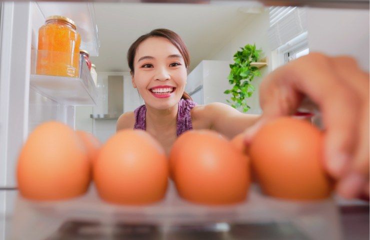 Donna che raccoglie uova dal frigo