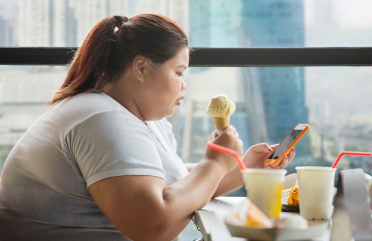 Donna obesa che mangia con lo smartphone