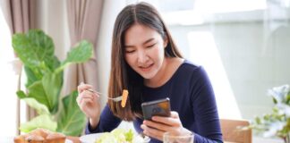 Ragazza che mangia consultando lo smartphone