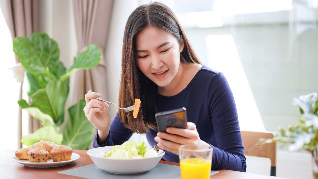 Ragazza che mangia consultando lo smartphone