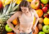 Una donna che tocca i suoi fianchi e della frutta come sfondo