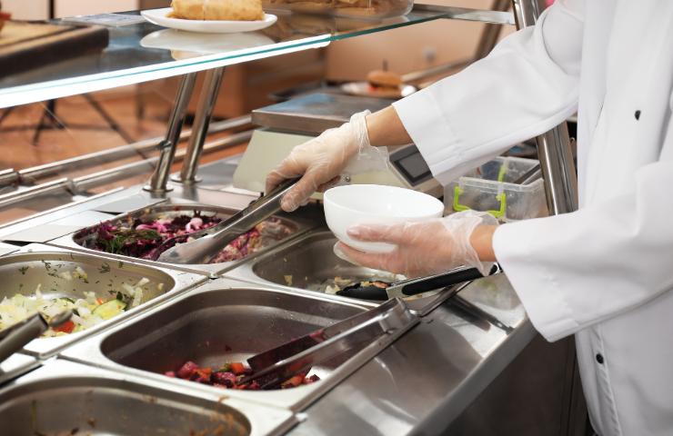 Un inserviente che serve del cibo in una mensa
