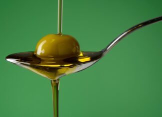 Olio extravergine versato su una oliva e su un cucchiaio