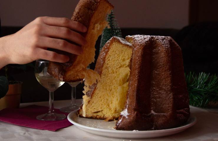 Mano che raccoglie una fetta da un pandoro tagliato - ricettasprint.it